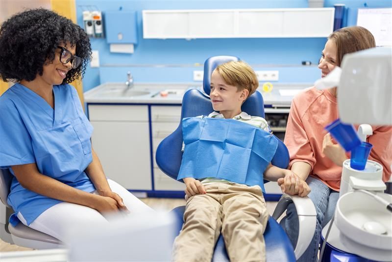 A boy with his mother at the dentist smiling.