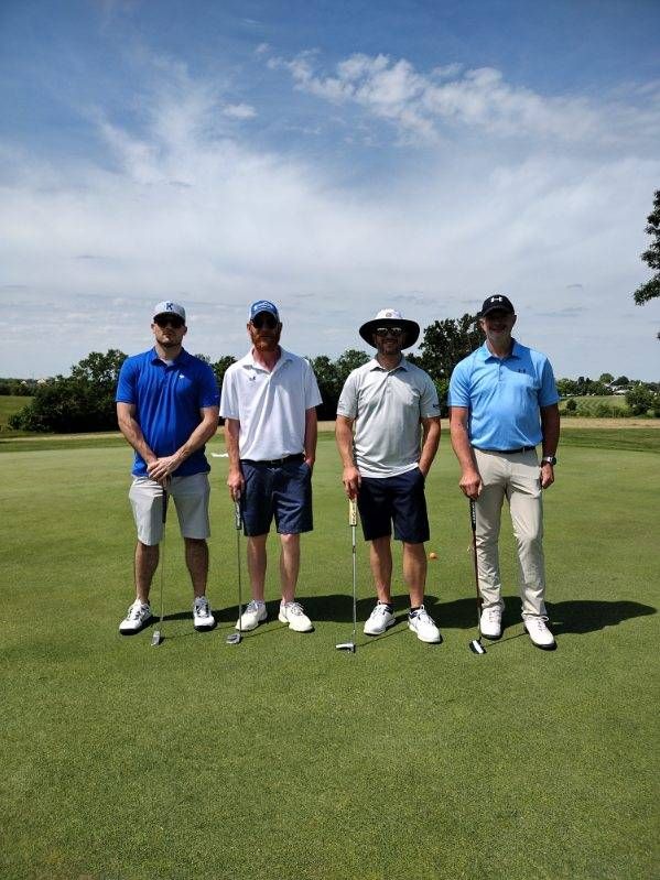 Four men are standing on a golf course holding golf clubs.