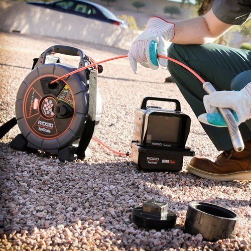 A person is kneeling down next to a hose reel and a camera.