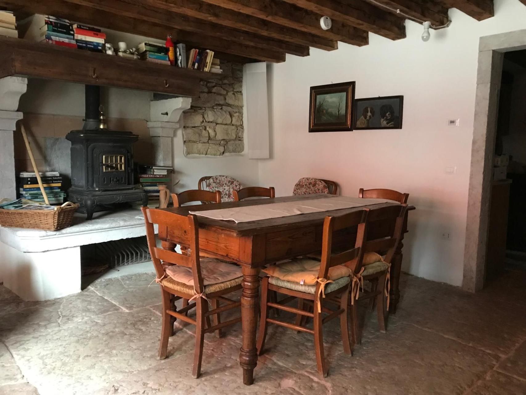 Sala da pranzo con tavolo e sedie in legno, camino in pietra con stufa e opere d'arte alle pareti.