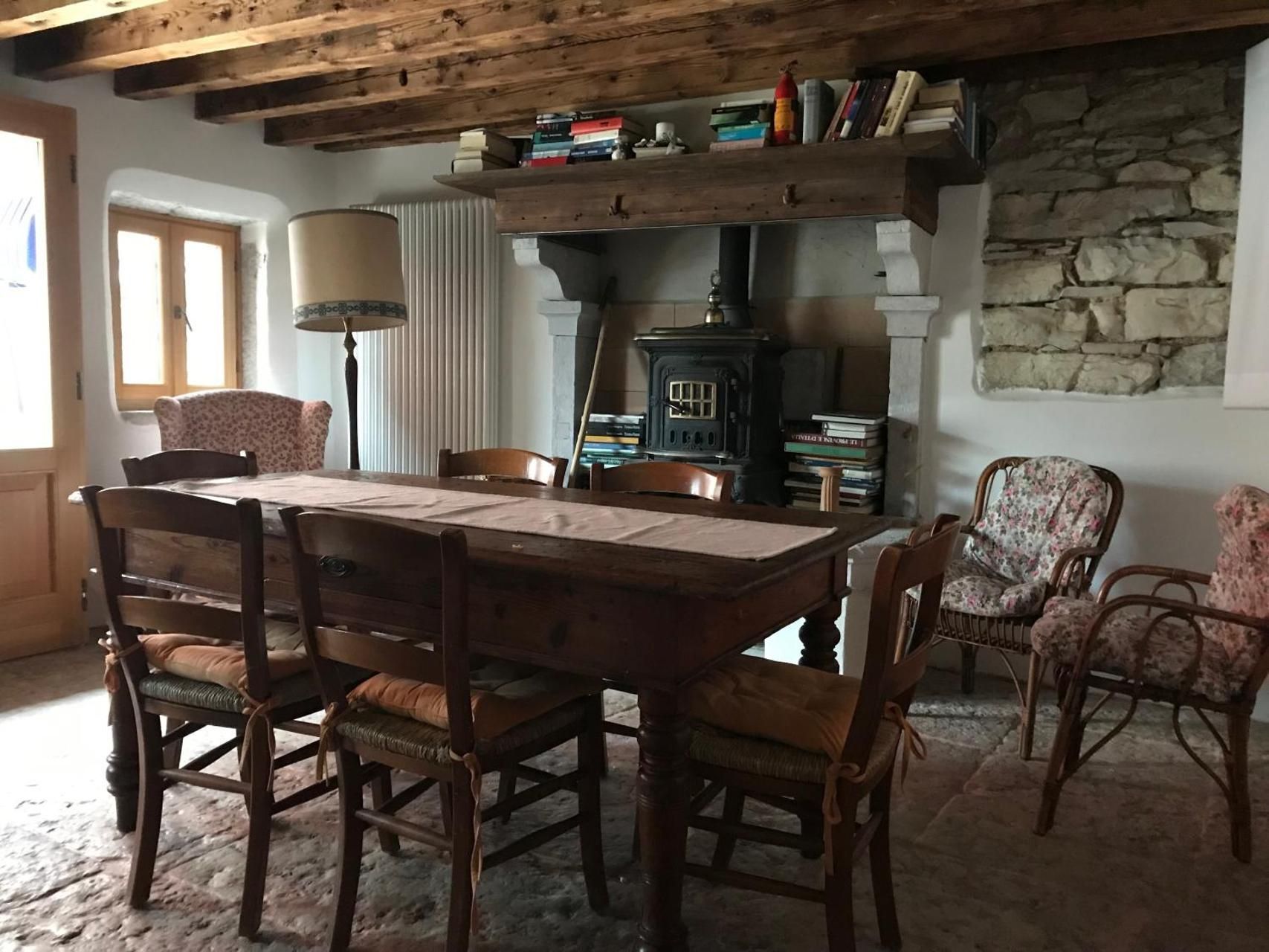 Sala da pranzo con tavolo in legno, sedie, camino e travi a vista.