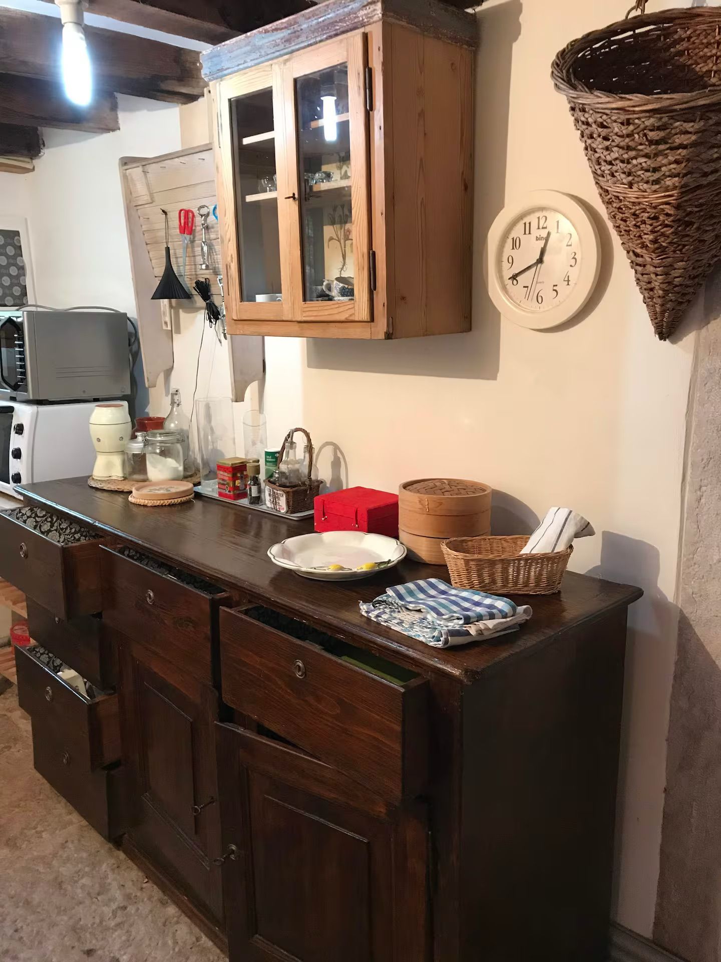 Mobile da cucina in legno con cassetti aperti, mobiletto sospeso e orologio sulla parete bianca.