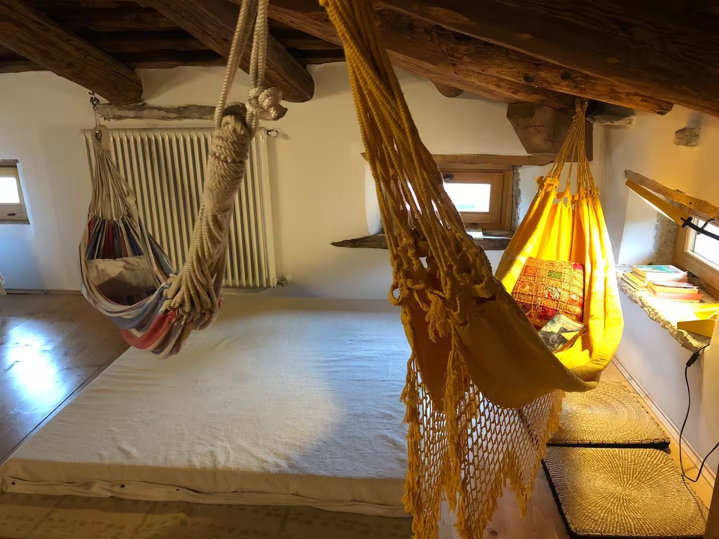 Accogliente mansarda con due amache sospese su un grande materasso. Travi in ​​legno.