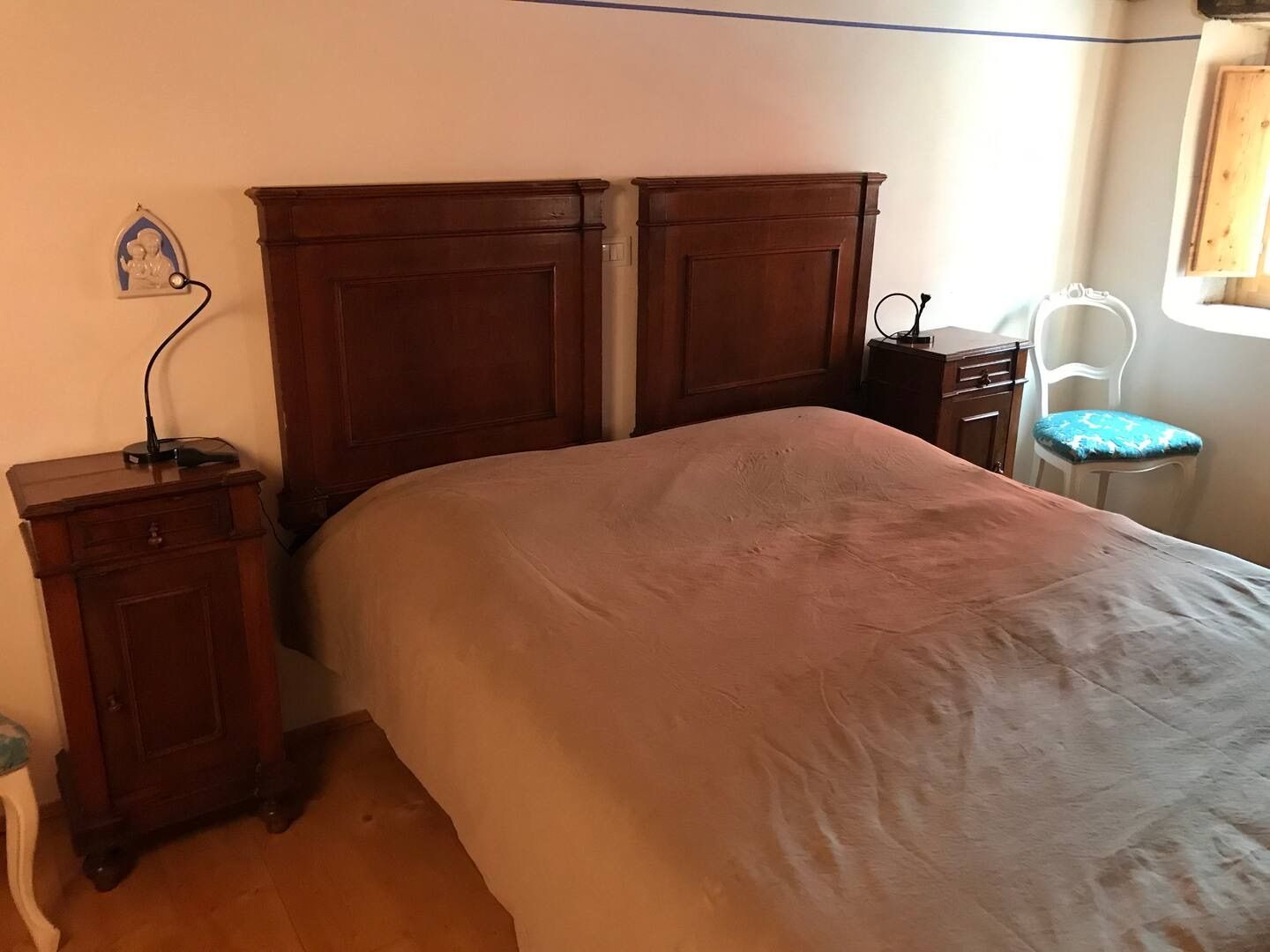 Camera da letto con grande testiera in legno, comodini, letto, sedia e piccola finestra.