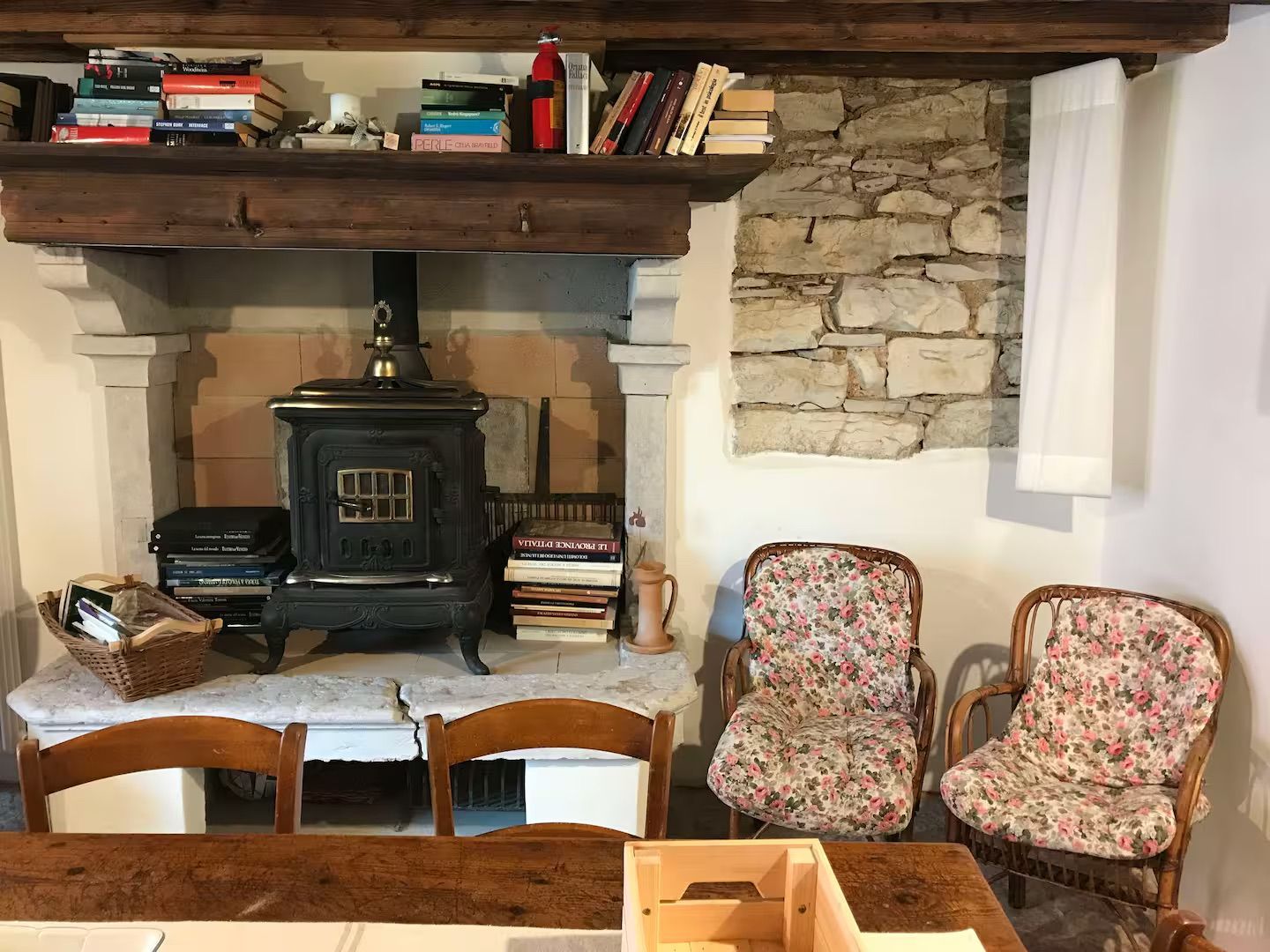Interni accoglienti con camino, libri, muro in pietra, sedie e un tavolo in legno.