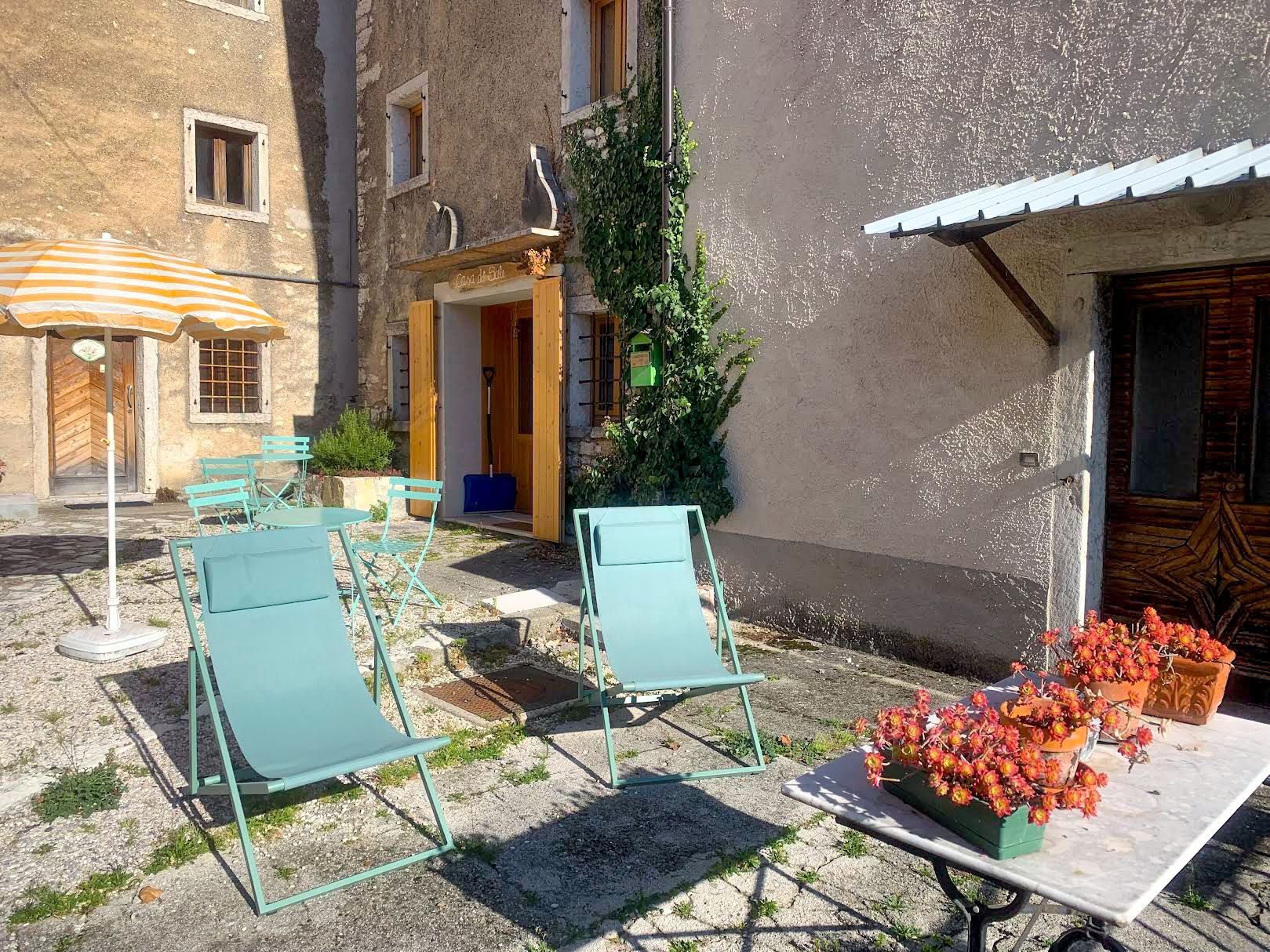 Due sedie pieghevoli blu su un patio, con un tavolo con piante in vaso, di fronte a un edificio.