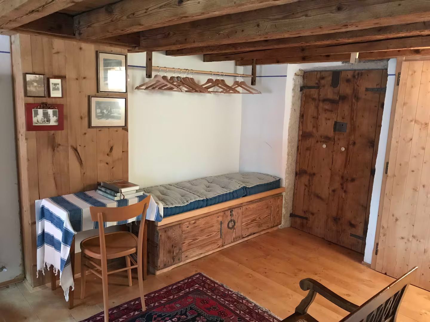 Camera accogliente con pannelli in legno, una panca con cuscini, un tavolino, un tappeto e una porta in legno.