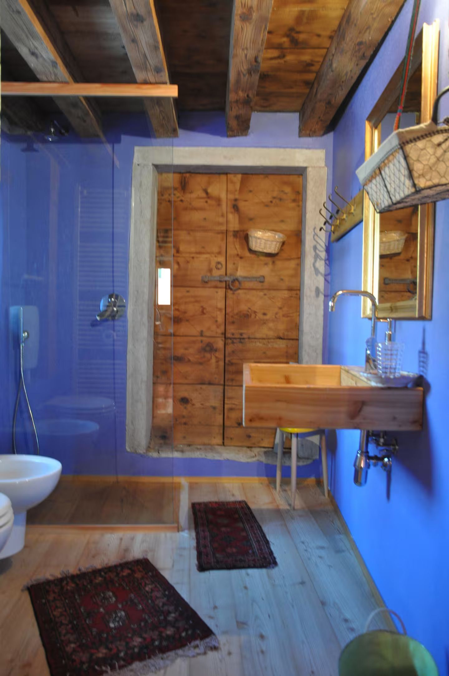 Bagno blu con porta, lavandino e travi in ​​legno rustico. Tappeti sul pavimento in legno.