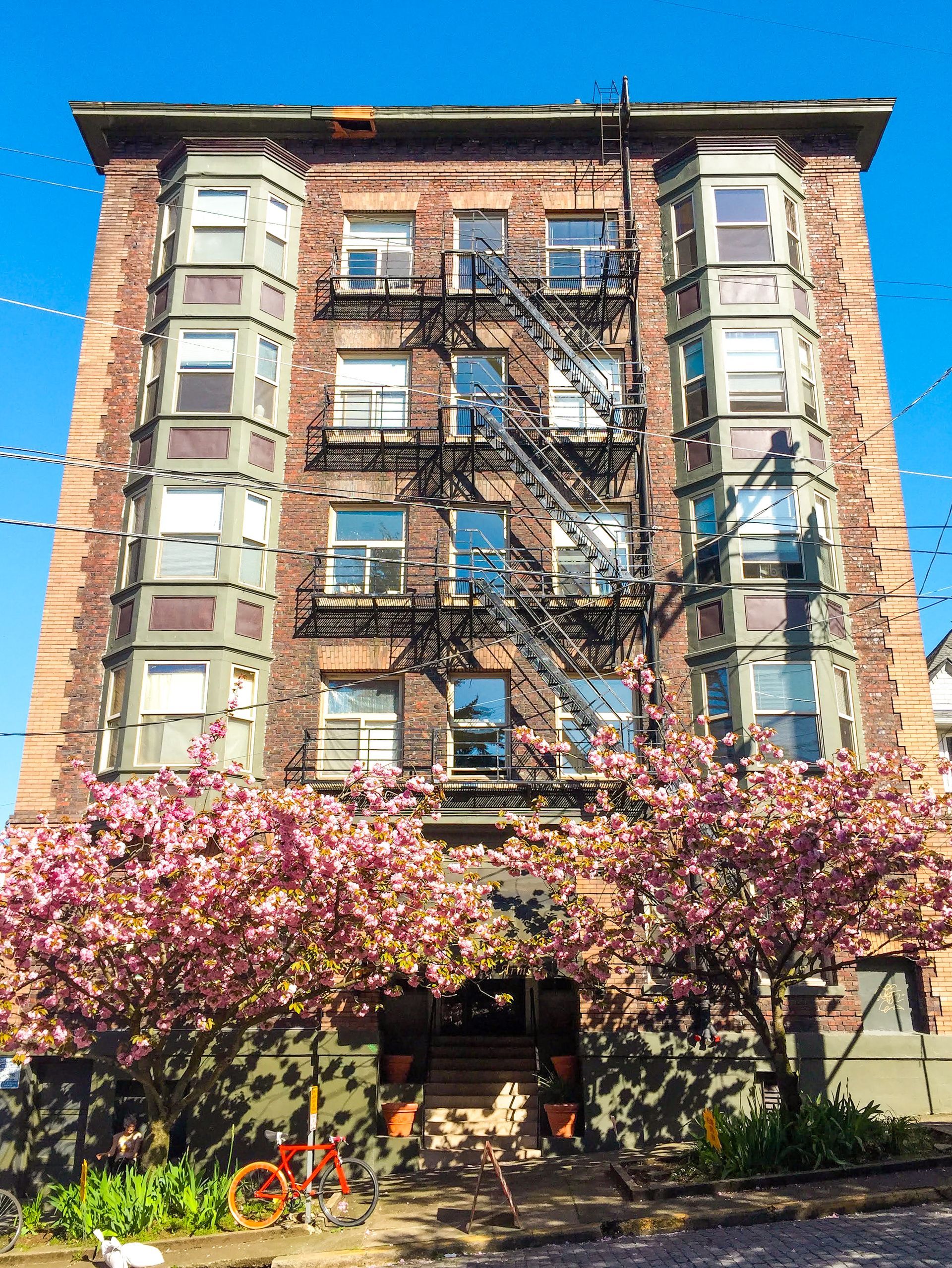 A large brick building with a fire escape and flowers in front of it.