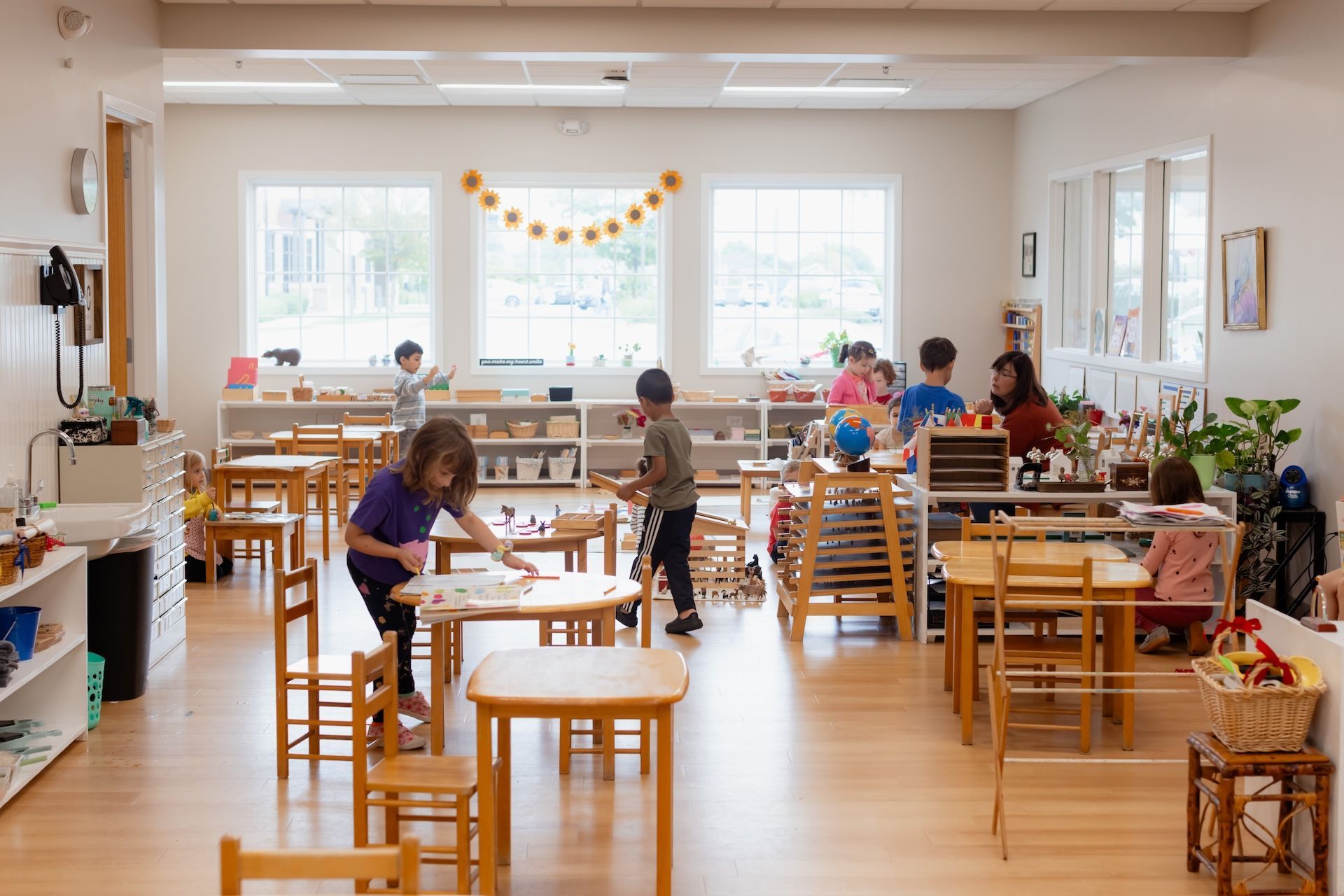 A group of children are playing in a classroom with tables and chairs.