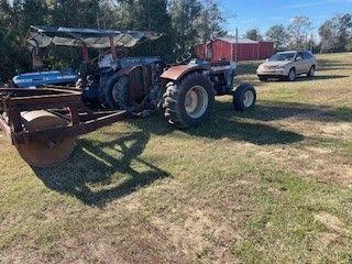 A tractor is pulling a trailer in a field next to a car.