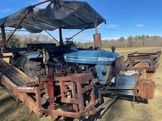 A blue tractor is parked in a field under a canopy.