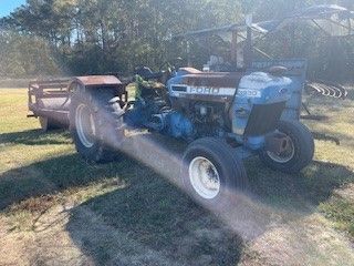 A blue tractor with a trailer attached to it is parked in a field.