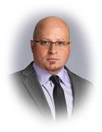Bald man wearing glasses, suit, and tie, looking forward.