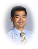 Smiling man wearing a light blue striped shirt and patterned tie.
