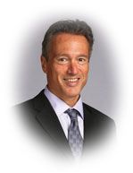 Smiling man in suit and tie, against a blurred background.