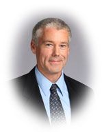 Man in suit and tie, smiling, against a blurred background.