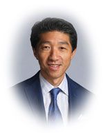 Smiling man in a blue suit and tie, against a blurred white and blue background.