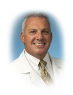 Man in white coat, smiling, against a blue backdrop.