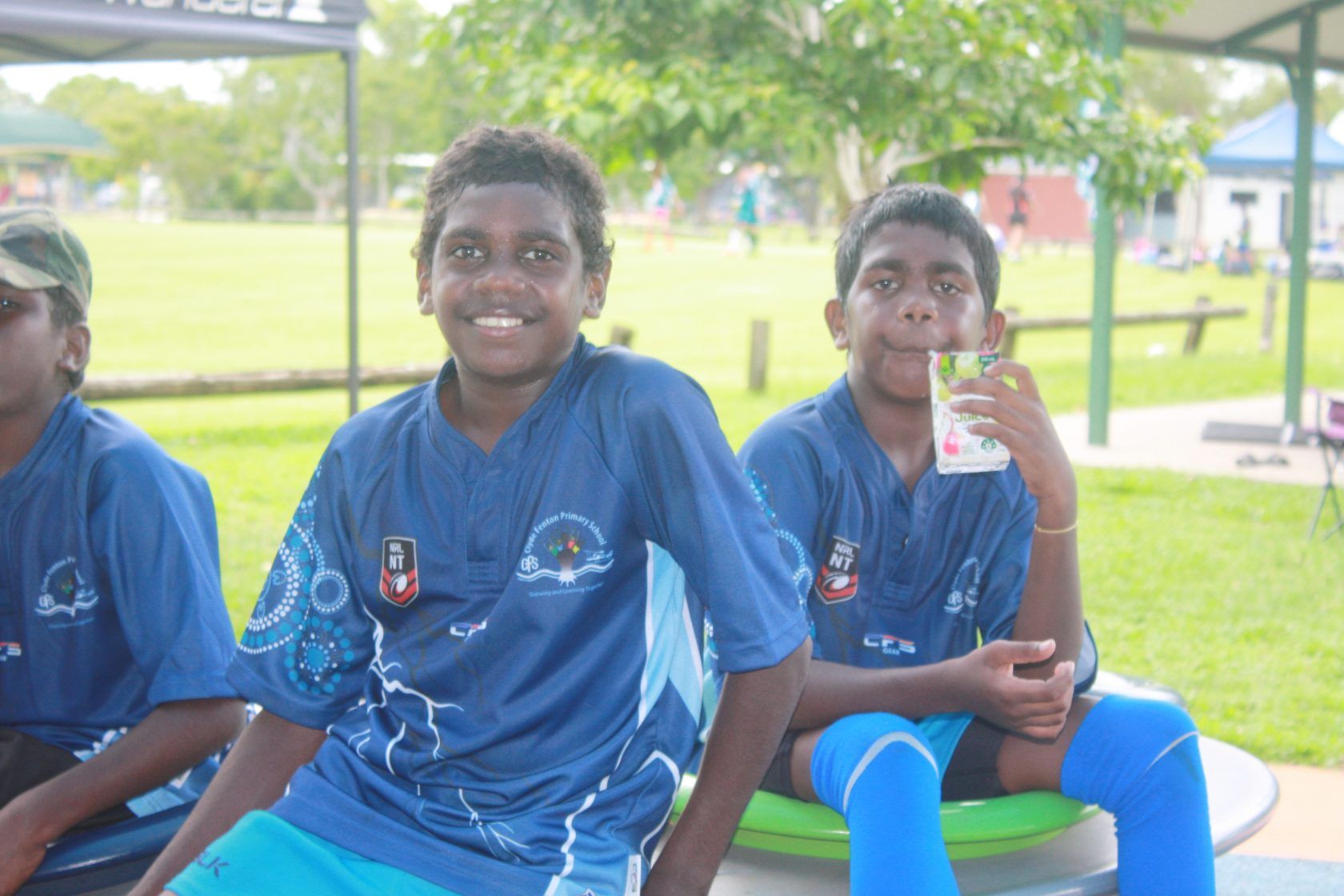 A group of young boys are sitting on a picnic table in a park.