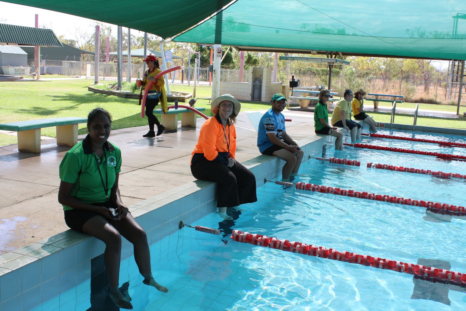 A group of people are sitting on the edge of a swimming pool.