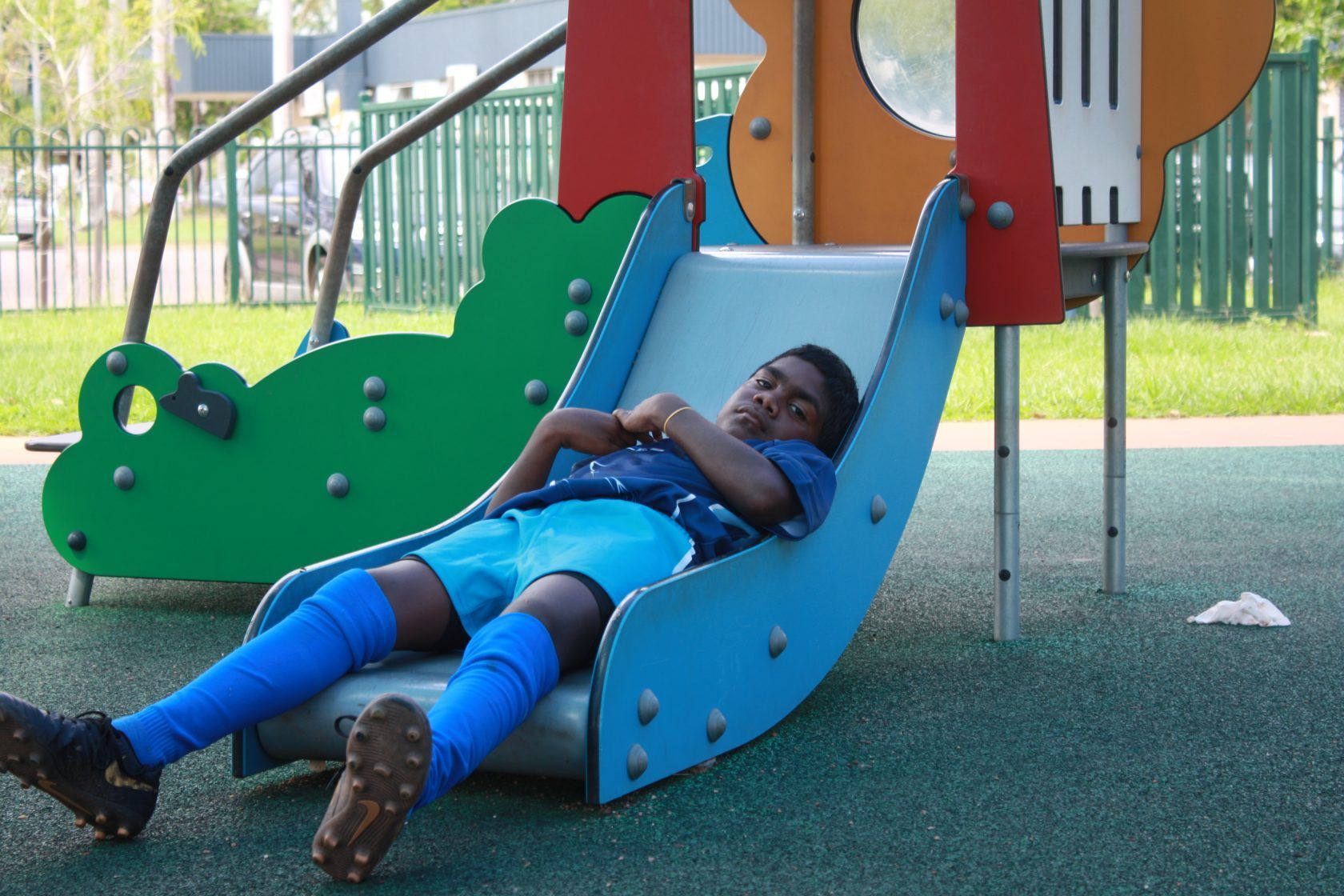 A young boy is laying on a slide at a playground