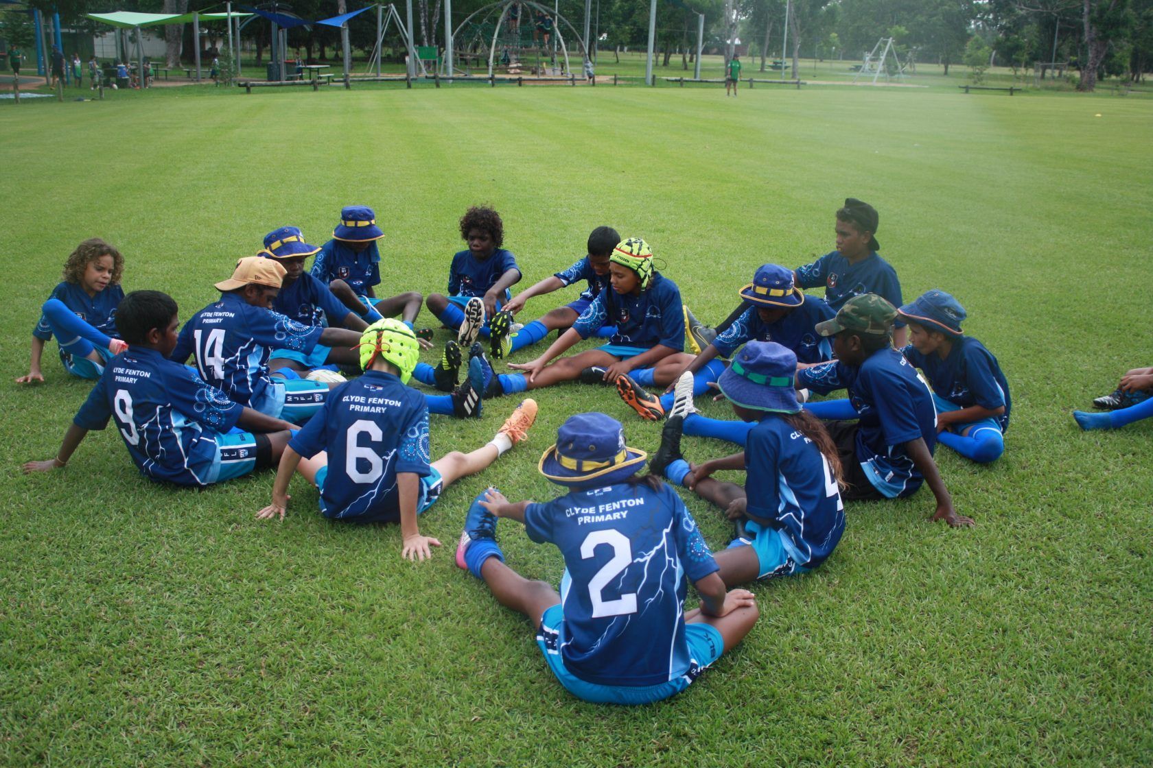 A group of children are sitting in a circle on the grass.
