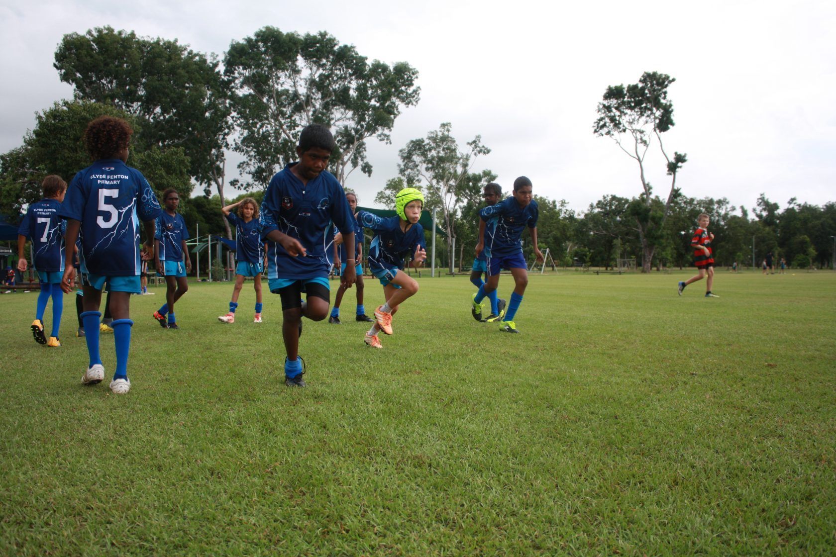 A group of children are playing soccer on a field and one of them has the number 5 on his shirt