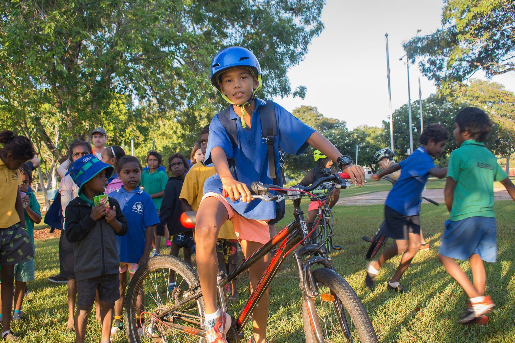 A boy wearing a blue helmet is riding a bike in front of a group of children.