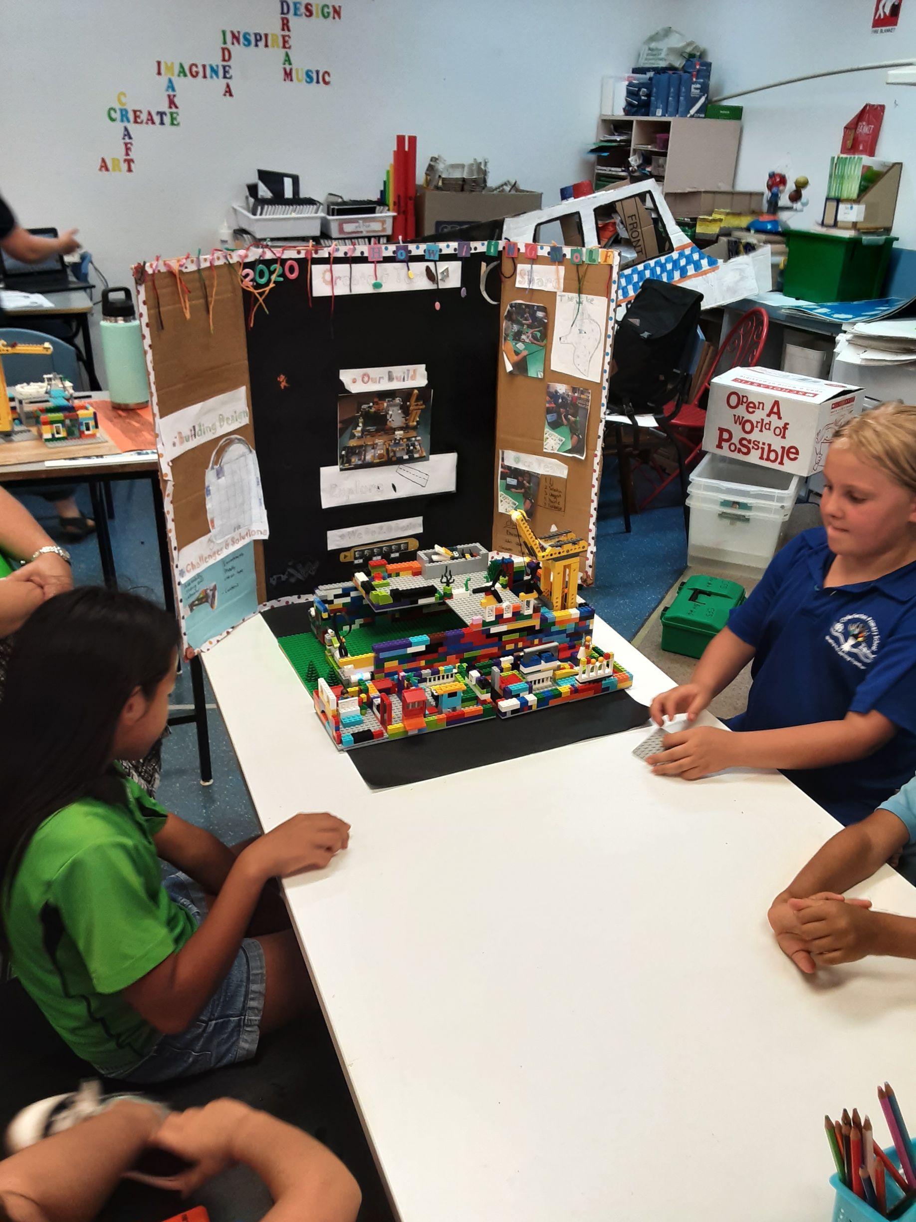 A group of children are sitting around a table with a lego model on it.