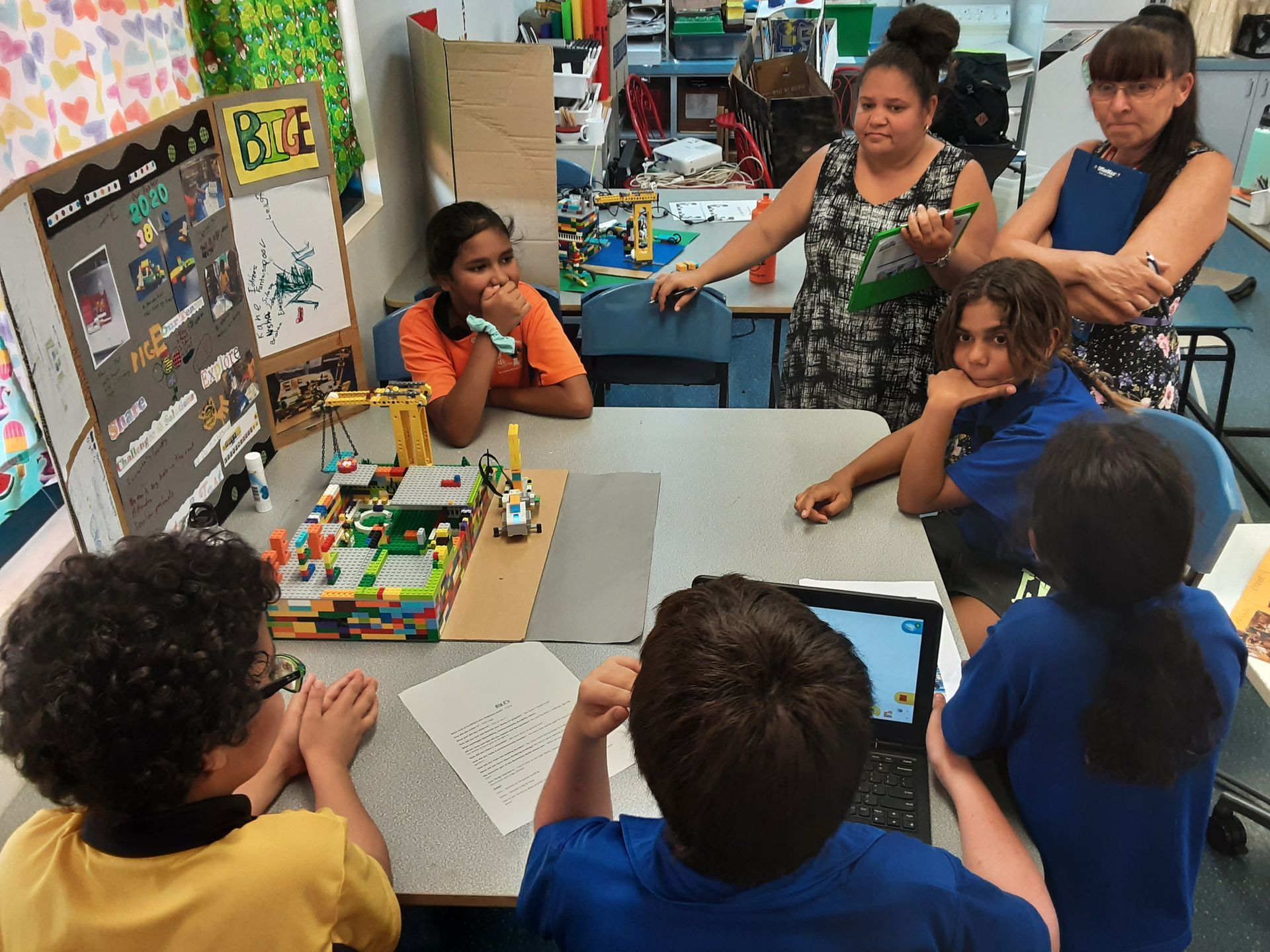 A group of children are sitting around a table with a sign on the wall that says recycle