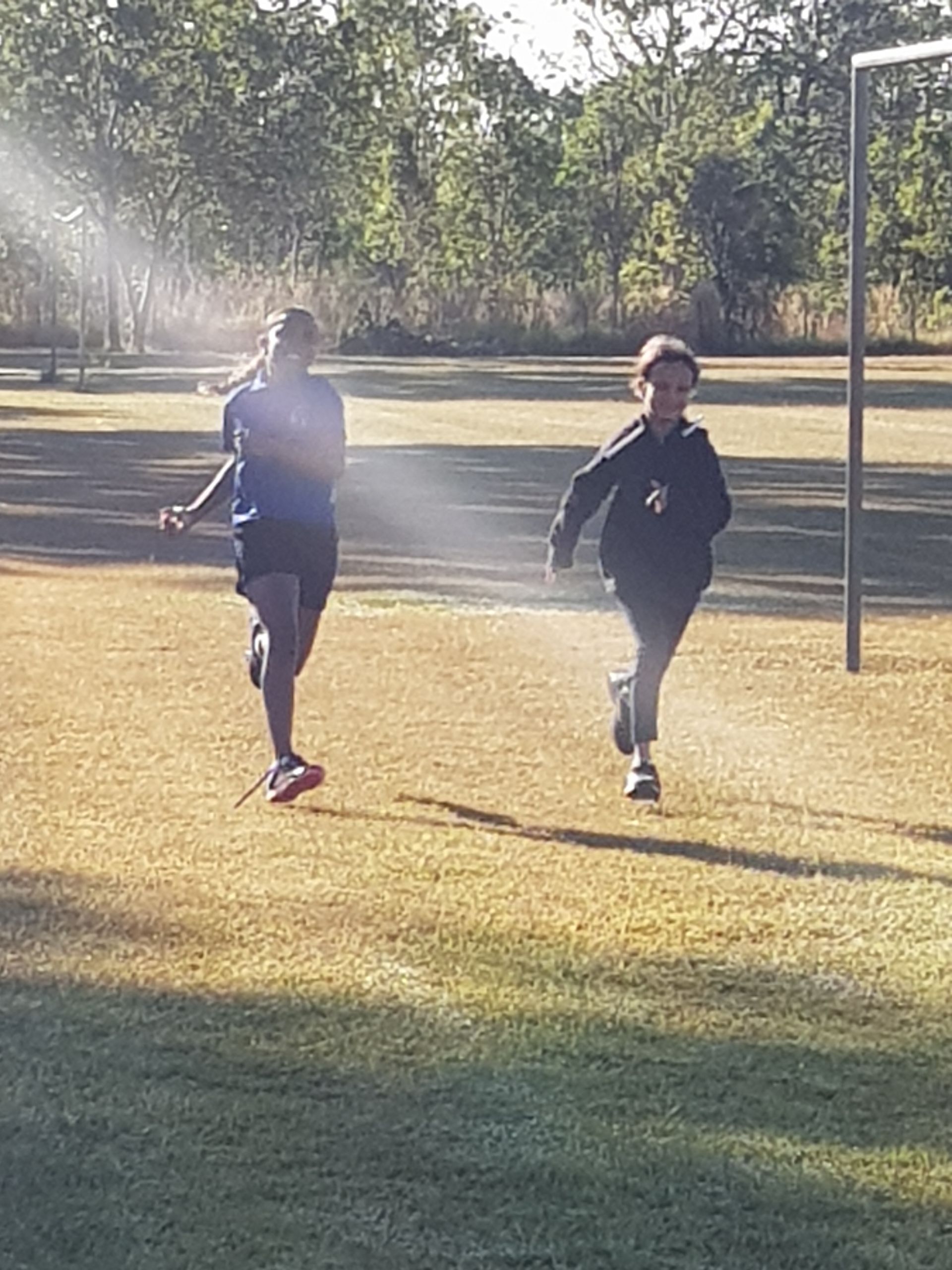Two people are running on a field with trees in the background.