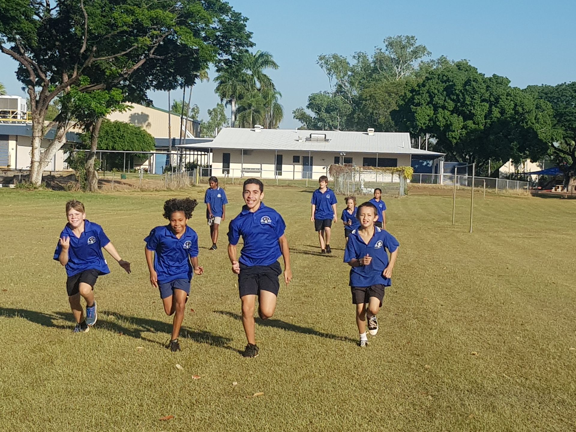 A group of children in blue shirts are running in a field