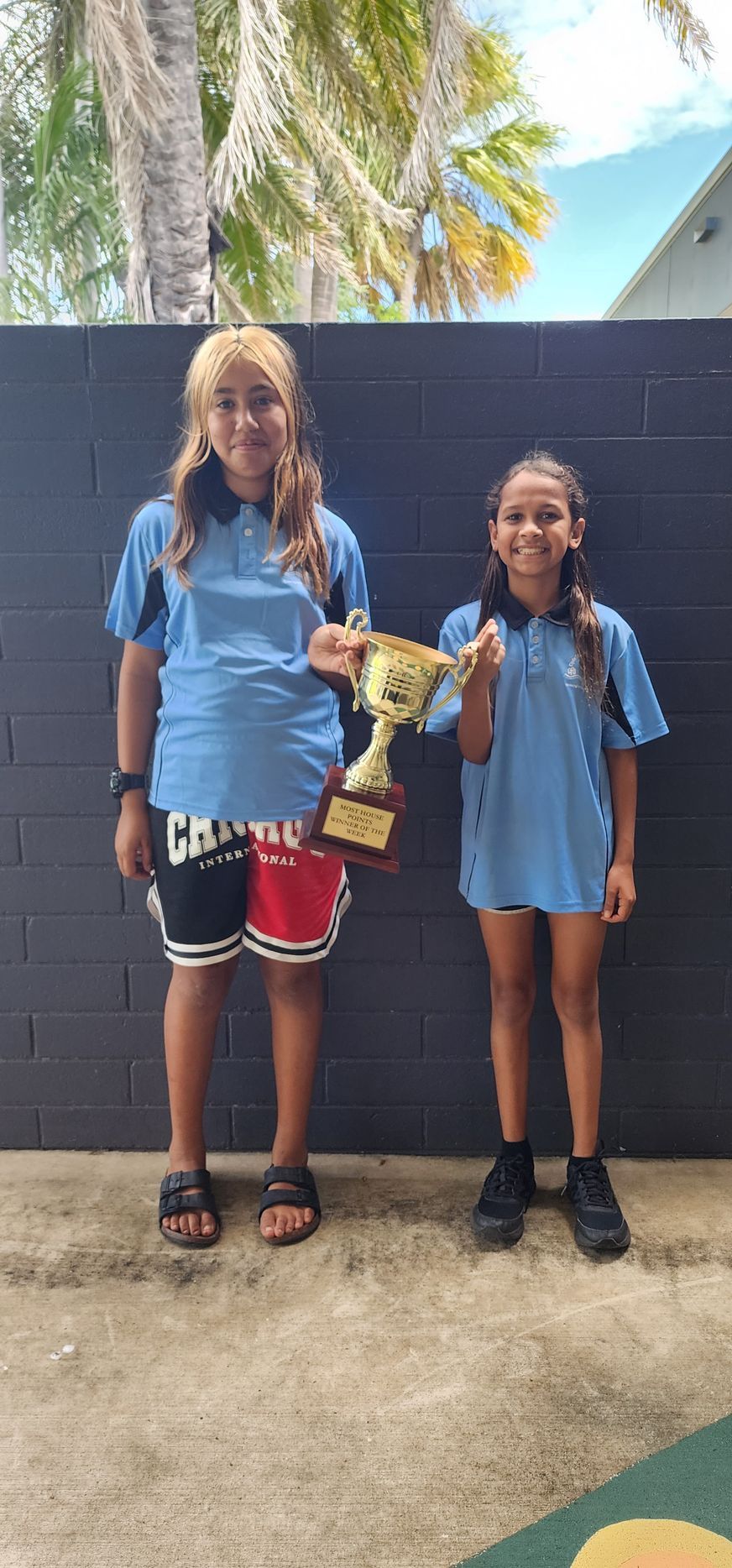 Two young girls are standing next to each other holding a trophy.