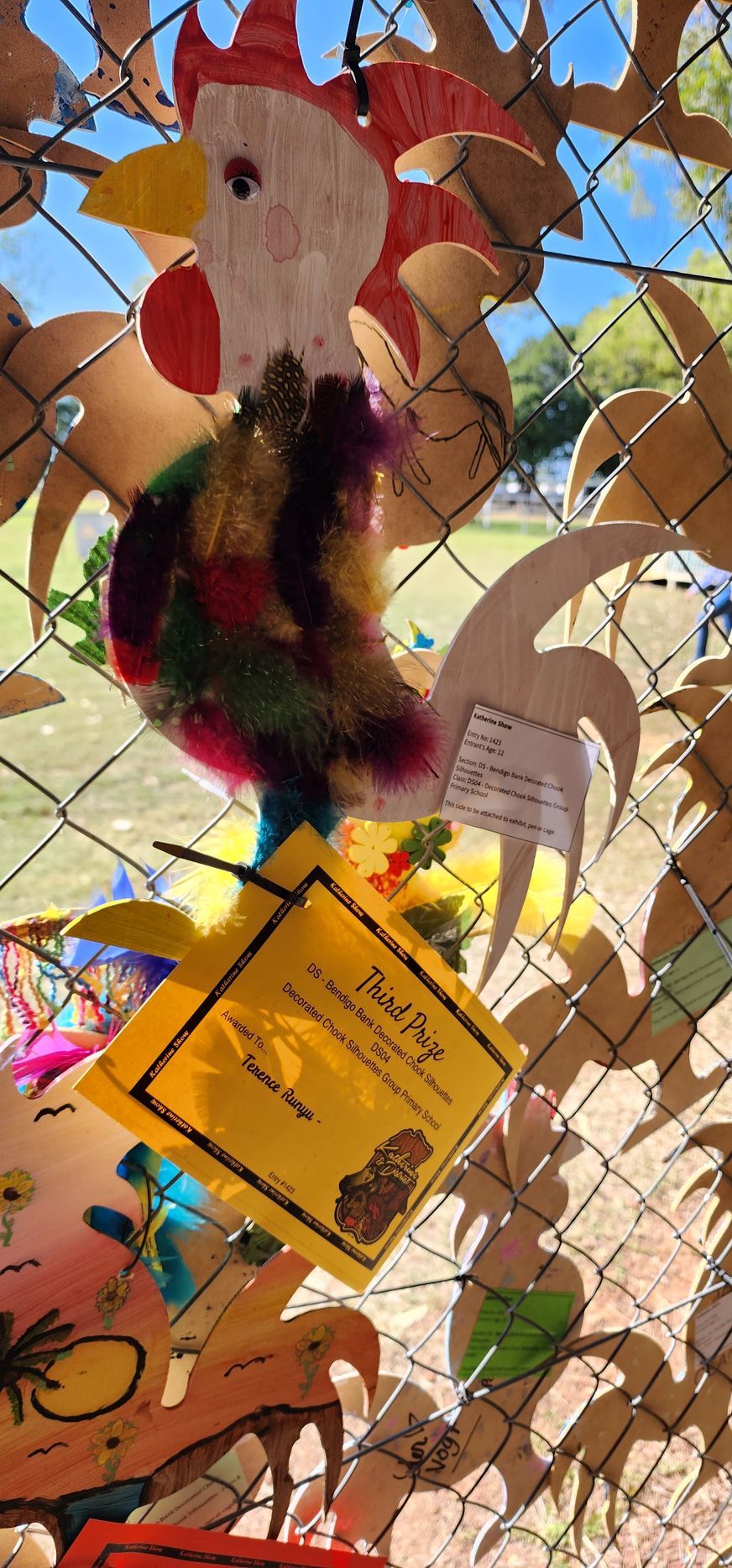A rooster made out of eggs is hanging from a chain link fence.