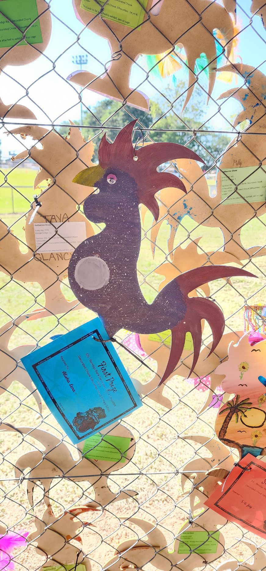 A rooster is hanging from a chain link fence.