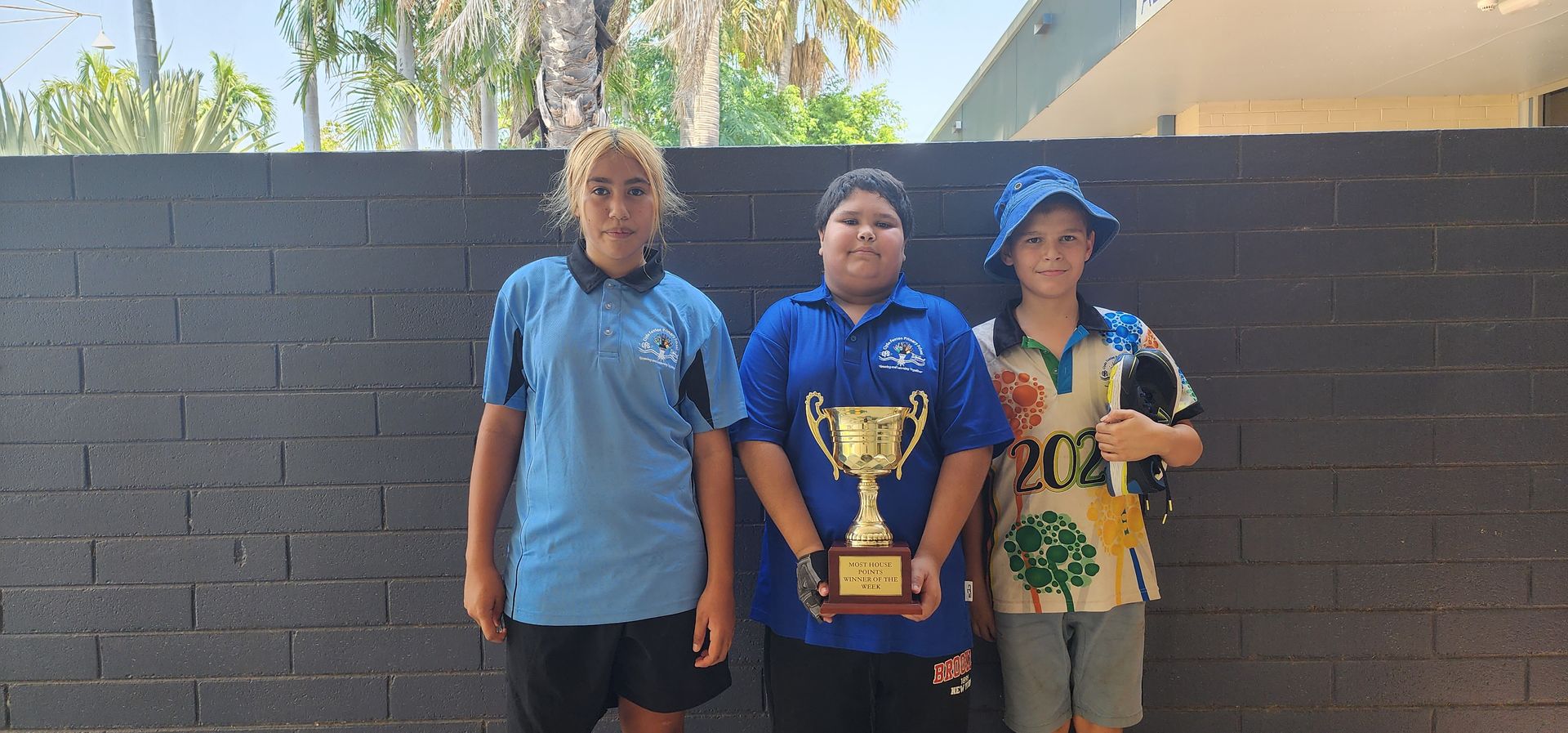Three young boys are standing next to each other holding a trophy.