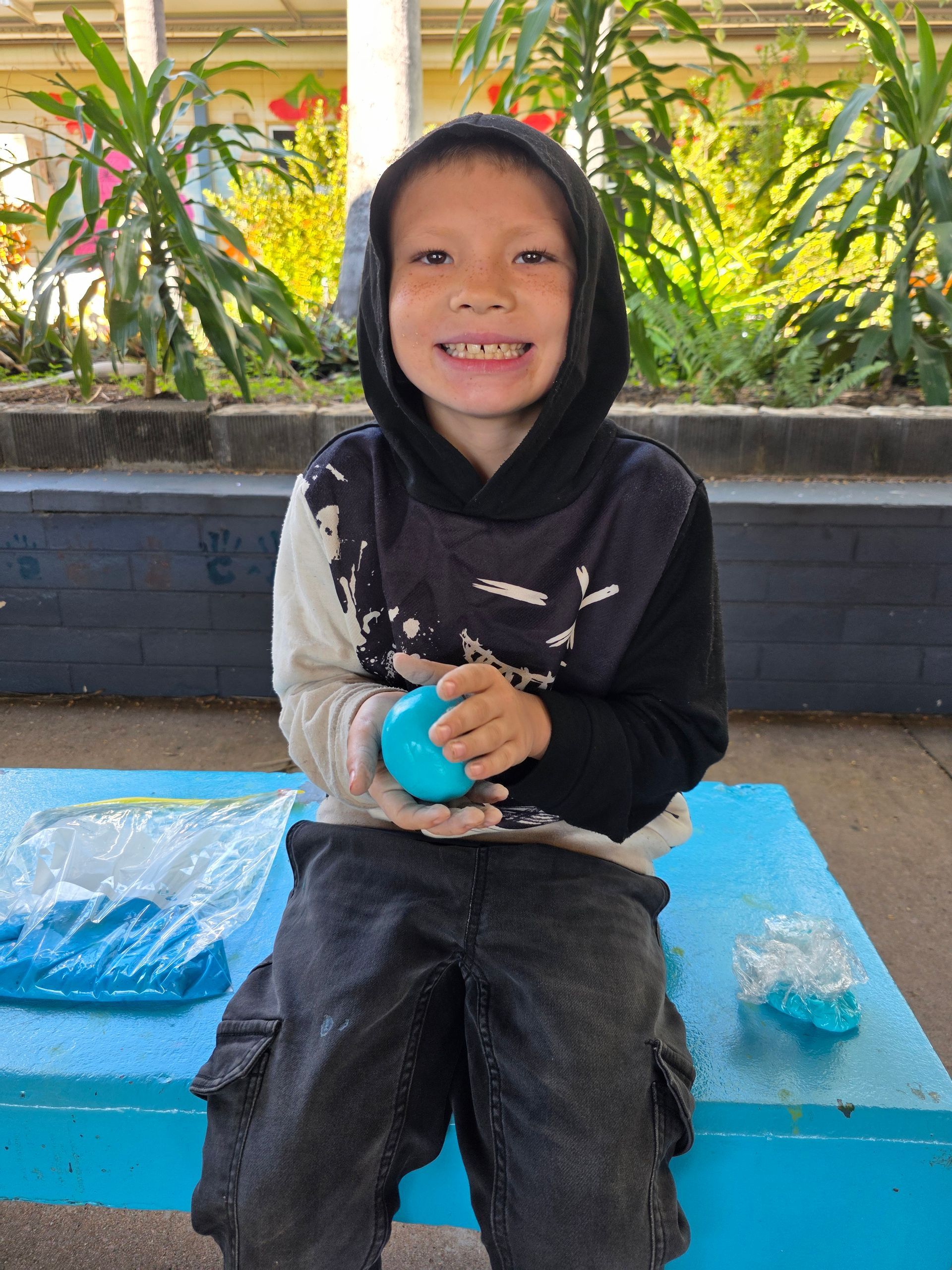 A young boy is sitting on a blue bench holding a blue ball