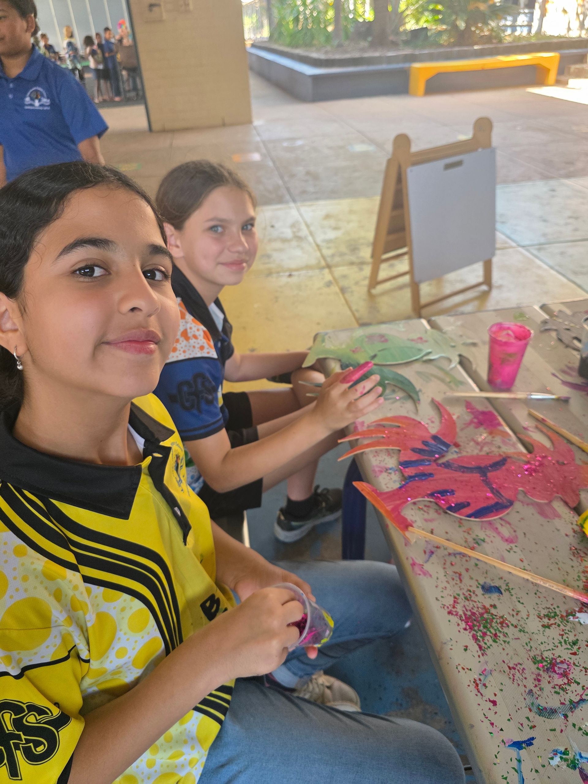 A girl in a yellow shirt is sitting at a table with other children