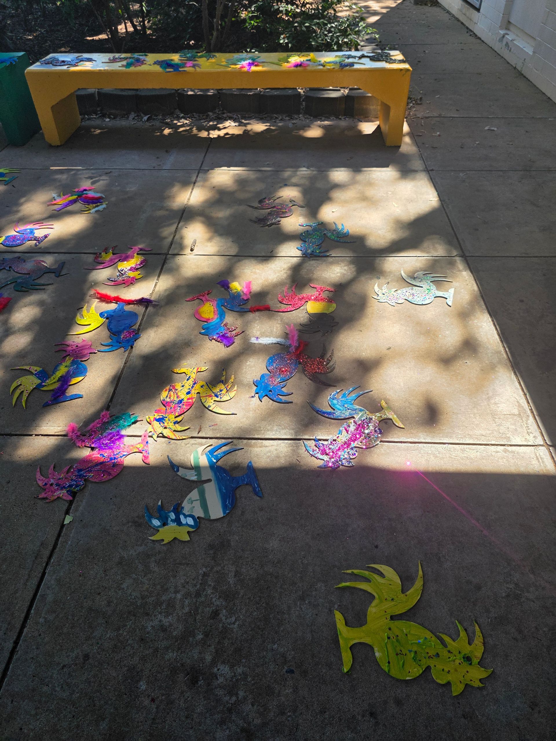 A yellow bench is sitting on a sidewalk surrounded by colorful decorations.