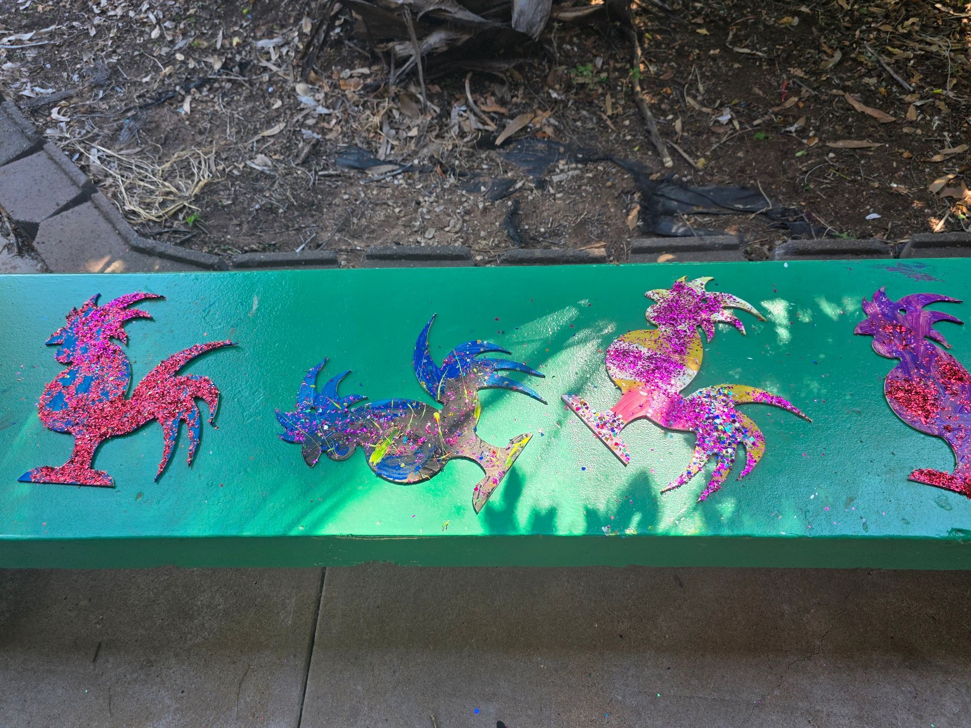 A green bench with roosters painted on it