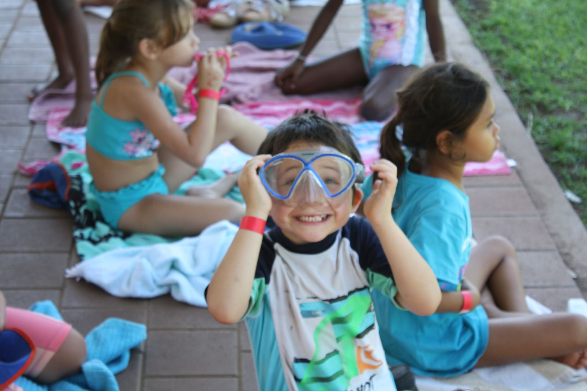 A group of children are sitting on towels wearing goggles
