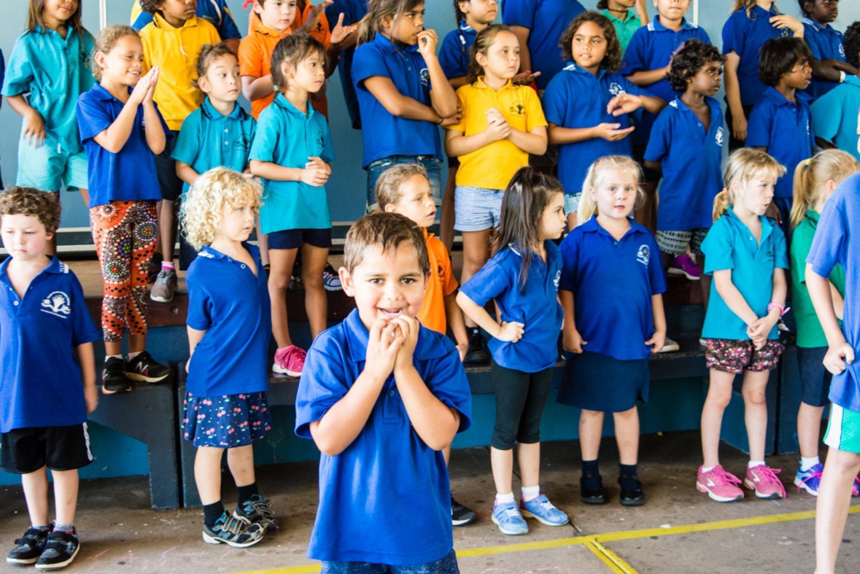 A boy in a blue shirt is standing in front of a large group of children.