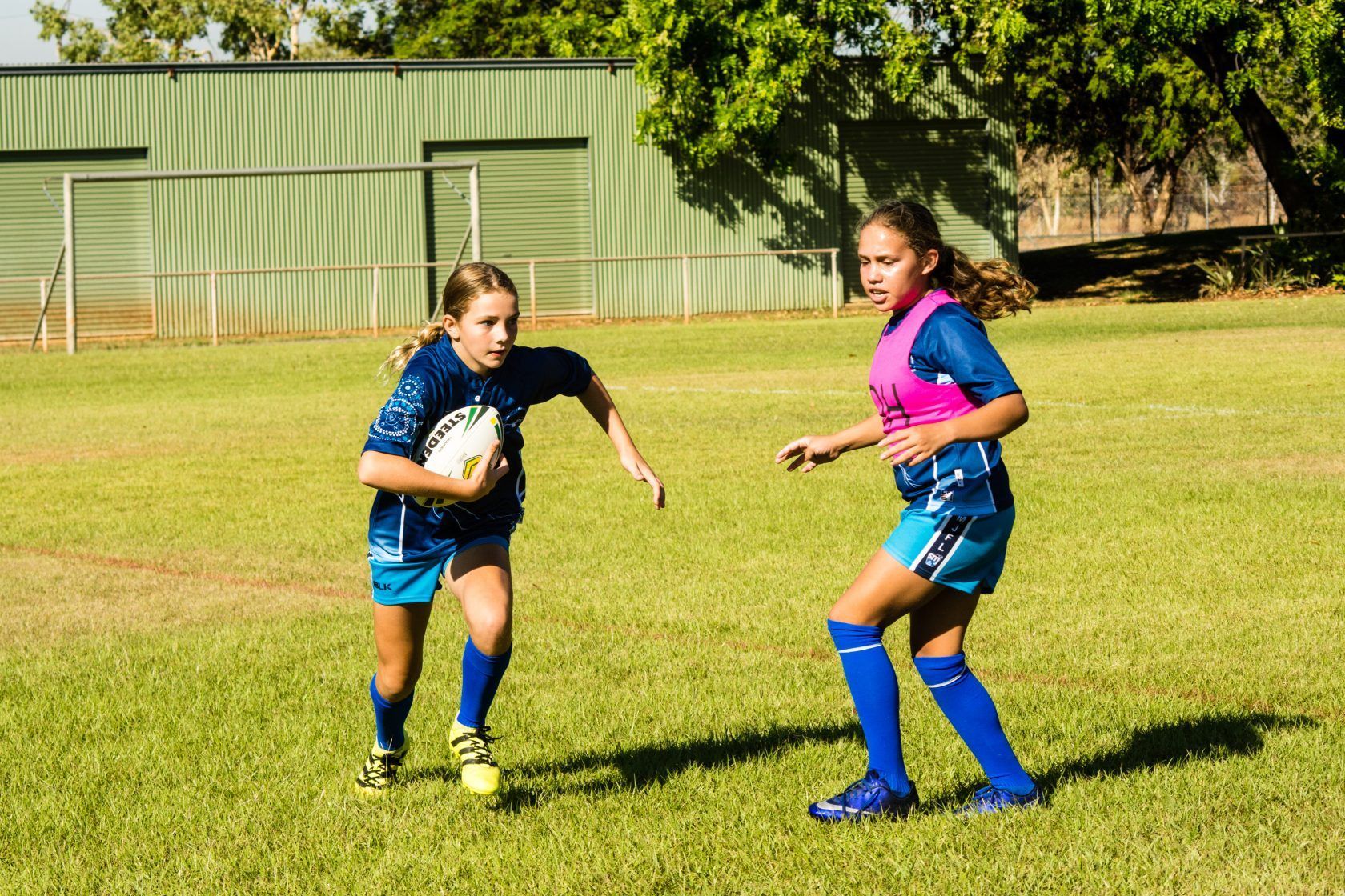 Two young girls are playing rugby on a field.