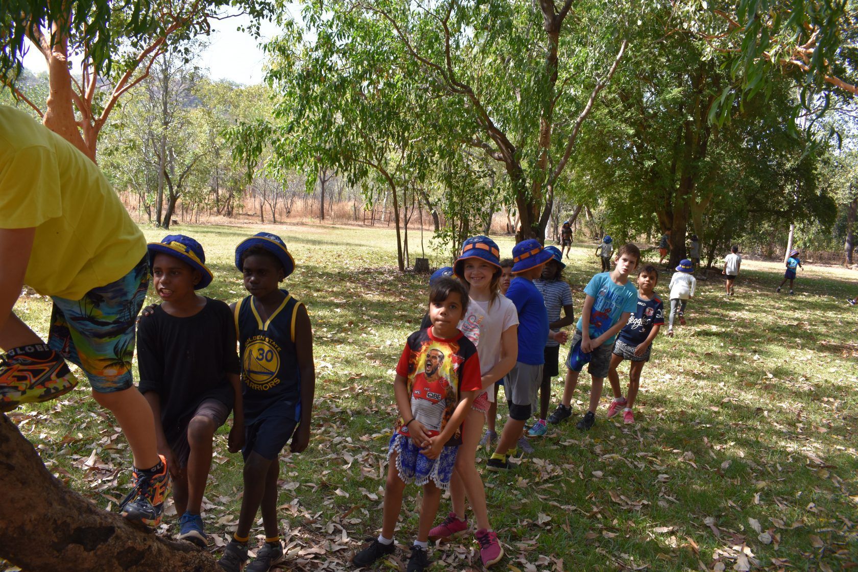 A group of children are standing on a tree branch in a park.