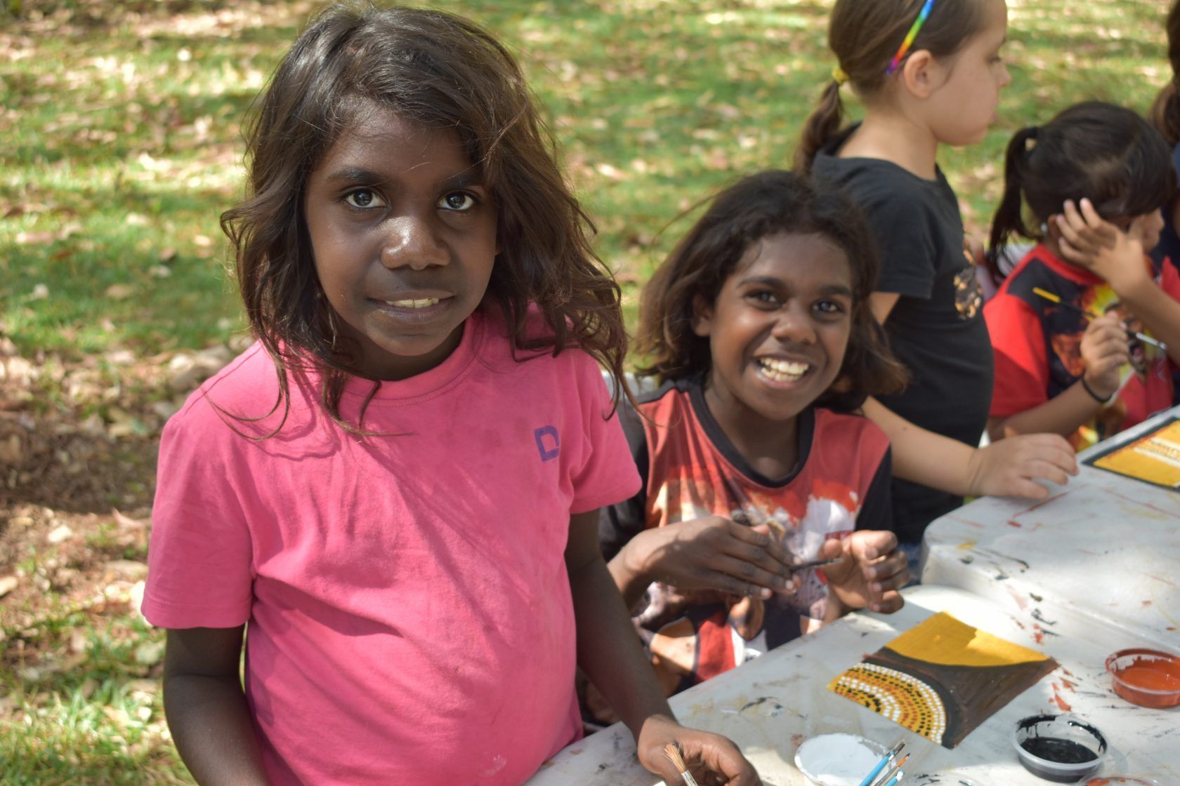 A girl in a pink shirt is sitting at a table with other children.