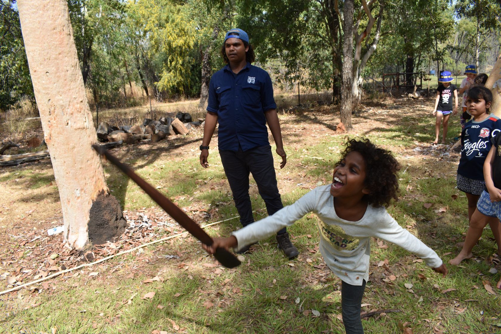 A girl is throwing a stick in the air while a man watches.