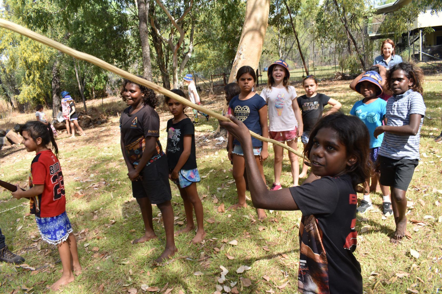 A group of children are standing in the grass holding sticks.