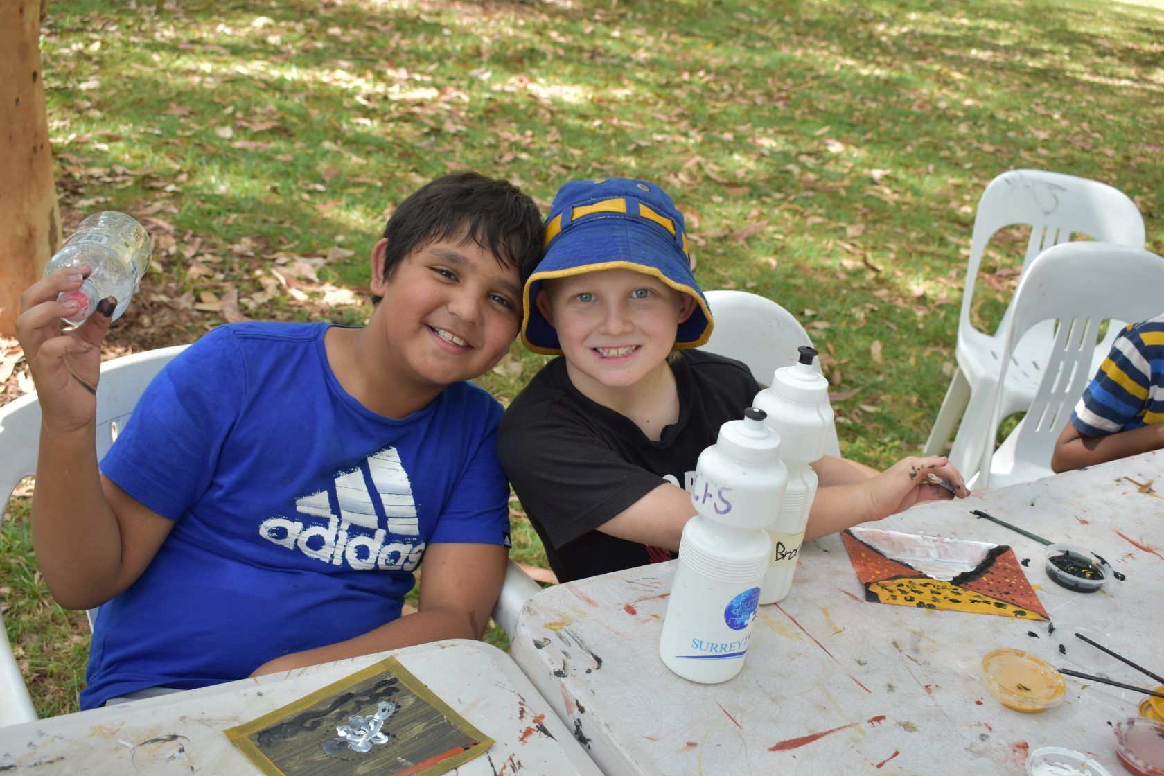 Two young boys are sitting at a table wearing adidas shirts