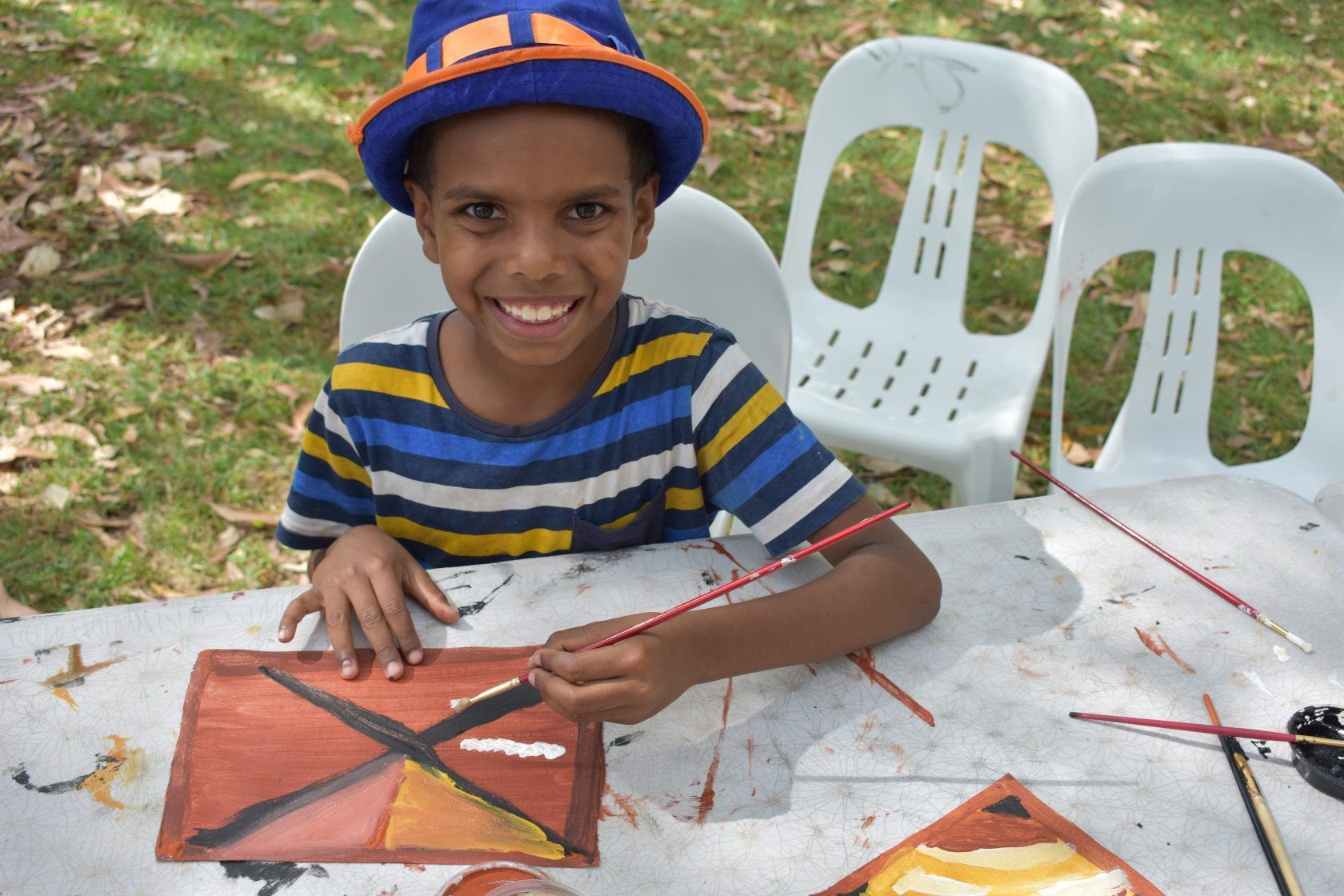 A young boy wearing a blue hat is sitting at a table painting